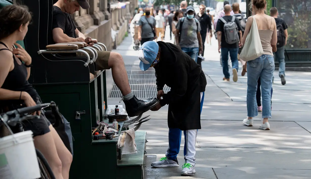 Seorang pria menyemir sepatunya pada hari yang hangat di New York City (7/6/2021). Cuaca yang hangat di New York dimanfaatkan warga untuk membaca buku hingga berjalan-jalan. (AFP/Angela Weiss)