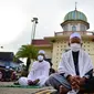 Pria-pria Muslim mengenakan masker dan duduk dengan menjaga jarak untuk melaksanakan salat berjemaah pada Idul Fitri yang menandai akhir bulan suci Ramadhandi halaman masjid Yakaniah di Narathiwat, provinsi selatan Thailand, 24 Mei 2020. (Photo by Madaree TOHLALA / AFP)