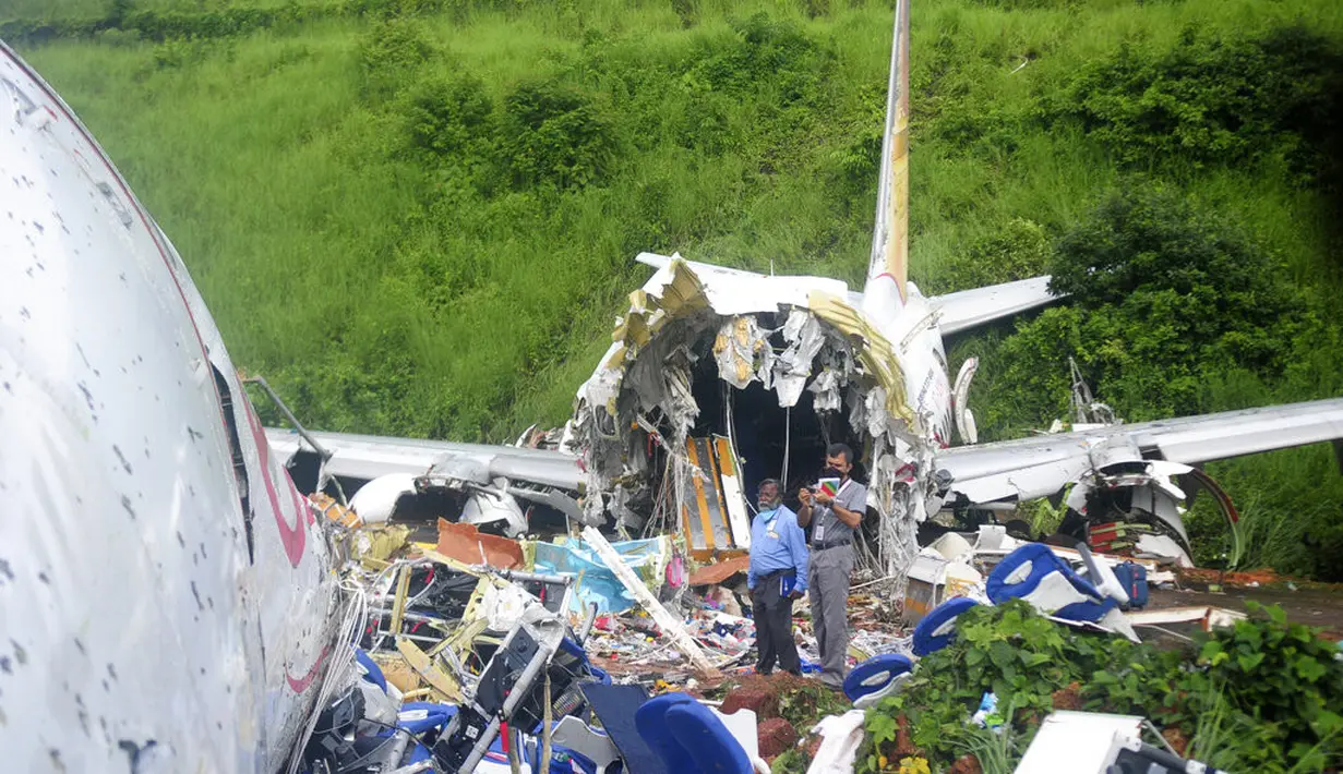 Petugas berdiri di atas puing-puing pesawat Air India Express yang tergelincir dari landasan pacu saat mendarat di Kozhikode, negara bagian Kerala, India, Sabtu, (8/8/2020). Pesawat Air India Express dengan 190 orang di dalamnya jatuh di sebuah bandara di negara bagian selatan Kerala. (AP Photo/C.K.