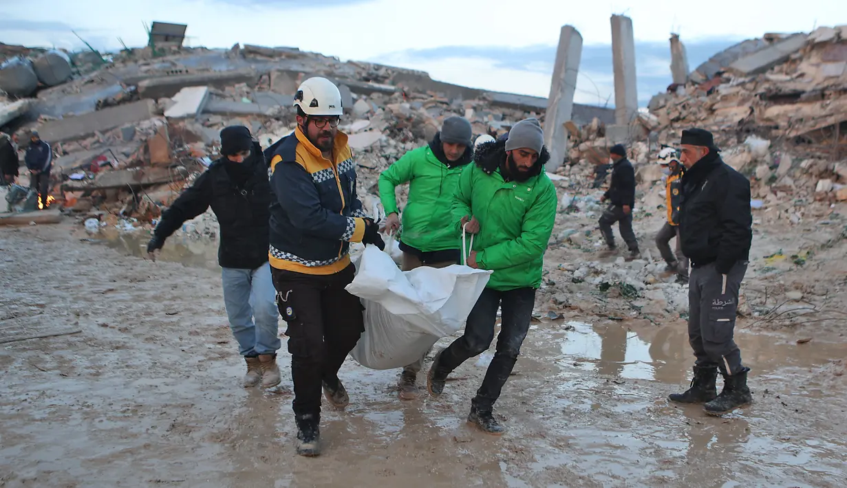 Penyelamat Suriah membawa jenazah melewati bangunan yang runtuh saat operasi pencarian berlanjut setelah gempa mematikan di kota Sarmada, di provinsi Idlib barat laut yang dikuasai pemberontak Suriah pada 6 Februari 2023. Setidaknya 1.400 orang tewas dan 3.411 terluka di seluruh Suriah hari ini dalam gempa bumi yang berpusat di Turki barat daya, kata pemerintah dan penyelamat. (AFP/Aaref Watad)