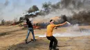 Dua pemuda Palestina berusaha menghalau dan melempar balik gas air mata yang ditembakkan oleh paskuan Israel di jalur Gaza (11/5). (AFP Photo/Mohammed Abed)