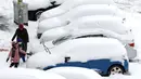 Penduduk setempat berjalan melewati mobil yang tertutup salju di Ankara, 23 Januari 2022.  Badai musim dingin dan hujan salju tetap berlaku di sebagian besar wilayah Turki, menyebabkan penutupan jalan antara ribuan desa dan kota di banyak daerah. (Adem ALTAN / AFP)
