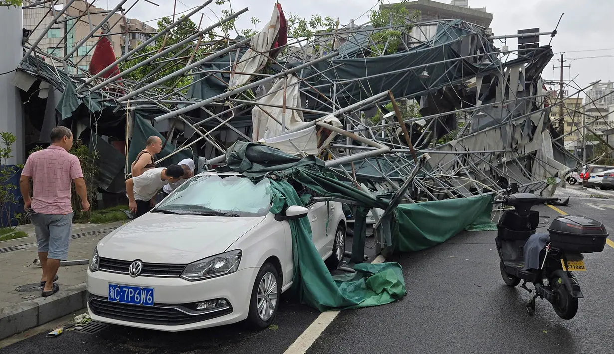 Warga melihat ke dalam sebuah mobil yang tertimpa struktur perancah yang roboh setelah Topan Dolphin melanda wilayah tersebut, di Wenzhou, Provinsi Zhejiang, Tiongkok timur, Senin, 10 Agustus 2026. (Chinatopix via AP)