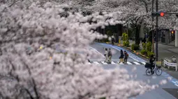Orang-orang berhenti untuk mengambil gambar saat mereka berjalan melintasi jalan bawah kanopi bunga sakura di Tokyo, Jepang, Minggu (27/3/2022). (AP Photo/Kiichiro Sato)
