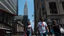Orang-orang berjalan melewati Gedung Chrysler pada hari yang hangat di New York City (7/6/2021). Cuaca yang hangat di New York dimanfaatkan warga untuk membaca buku hingga berjalan-jalan. (AFP/Angela Weiss)