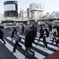 Orang-orang yang mengenakan masker pelindung untuk membantu mengekang penyebaran Virus Corona berjalan di sepanjang penyeberangan pejalan kaki di Tokyo (19/1/2021). Ibukota Jepang itu mengonfirmasi lebih dari 1.200 kasus Virus Corona baru pada 19 Januari 2021. (AP Photo/Eugene Hoshiko)