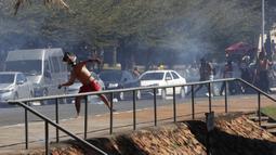 Seorang penduduk asli Brasil melempari polisi dengan batu saat demo menentang RUU Reformasi Agraria di luar Kongres di Brasilia, Brasil, Selasa (22/6/2021). Penduduk asli Brasil menilai RUU Reformasi Agraria akan membatasi pengakuan lahan reservasi. (AP Photo/Eraldo Peres)