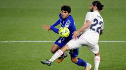 Gelandang Real Madrid, Isco, berusaha menghadang pemain Getafe, Carles Alena, pada laga Liga Spanyol di Stadion Alfonso Perez, Senin (19/4/2021). Kedua tim bermain imbang 0-0. (Photo by PIERRE-PHILIPPE MARCOU / AFP)