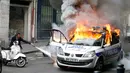 Petugas berusaha memadamkan mobil polisi yang terbakar akibat demo di Paris, Prancis (18/5). Demo buruh tersebut menentang kekerasan polisi dan melawan reformasi hukum yang berakhir bentrok dengan polisi. (REUTERS / Charles Platiau)