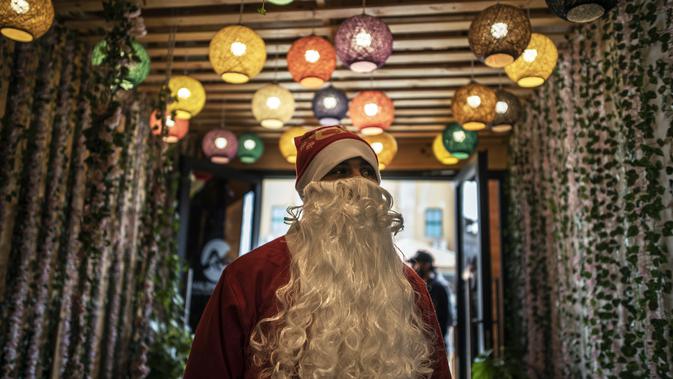Seorang pramusaji Palestina berpakaian berpakaian Sinterklas menyambut pengunjung di pintu masuk sebuah restoran di pantai di Kota Gaza, Minggu (13/12/2020). Restoran tersebut didandani dengan tema Natal, pelayanannya pun berpakaian seperti Sinterklas. (AP Photo/Khalil Hamra)