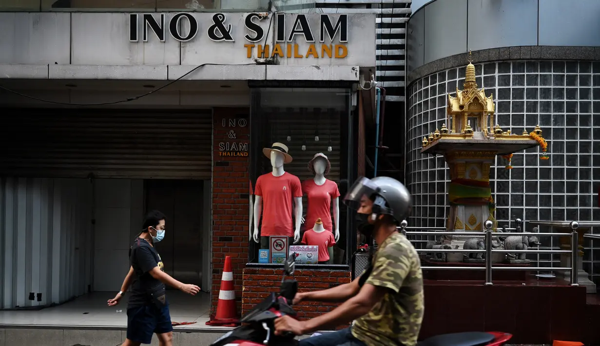 Orang-orang melewati toko-toko yang tutup di pasar grosir pakaian di Bangkok pada hari pertama penguncian COVID-19 yang lebih ketat, Senin (12/7/2021).  Thailand menerapkan lockdown untuk menekan laju penyebaran virus corona di Bangkok dan provinsi sekitarnya. (Lillian SUWANRUMPHA/AFP)