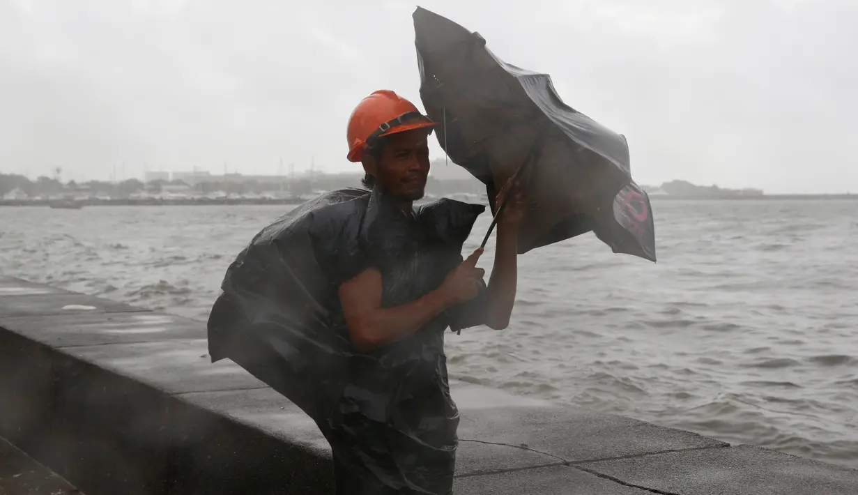 Seorang pria menahan payung yang tertiup angin kencang dan hujan ditengah cuaca buruk akibat Topan Nepartak yang menerpa kota Manila, Filipina, Jumat (8/7). (REUTERS/Erik De Castro)