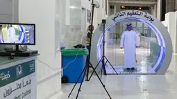 Seorang pria melewati gerbang sterilisasi mandiri yang didirikan di pintu masuk Ka'bah dan Masjid Haram selama bulan suci Ramadan di Mekkah pada 8 Mei 2020. Gerbang ini dipasang sebagai bagian dari tindakan pencegahan yang telah dilakukan sejak pecahnya Pandemi virus Corona (COVID-19). (STR / AFP)