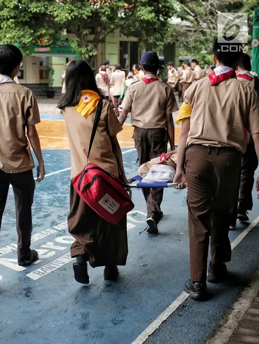 Sejumlah siswa menggotong temannya saat simulasi bencana di SMA Negeri 78 Jakarta Barat, Rabu (23/1). Kegiatan itu untuk pengenalan kepada siswa-siswi dengan program siaga bencana berupa simulasi evakuasi gempa dan tsunami. (Liputan6.com/Faizal Fanani)