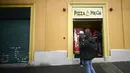 Orang-orang mengantre di mesin penjual pizza otomatis, yang pertama dari jenisnya di pusat kota Roma, Italia pada 29 April 2021. Mesin penjual otomatis ini mampu menguleni adonan, membumbui, memasak, dan menyajikan pizza dalam kotak karton hanya dalam waktu tiga menit. (Filippo MONTEFORTE/AFP)