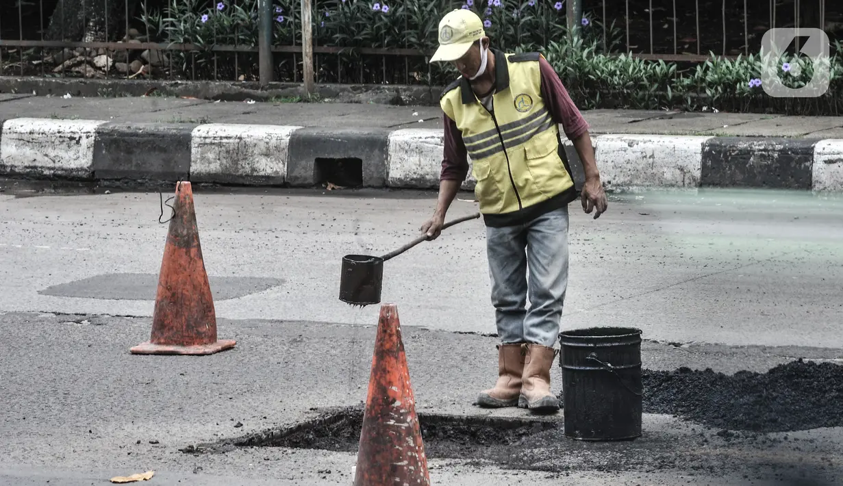 Petugas dari Dinas Bina Marga mengerjakan perbaikan jalan berlubang di Jalan DI Panjaitan, Cawang, Jakarta, Senin (25/1/2021). Perbaikan jalan rusak dan berlubang akibat sering tergenang banjir di kawasan tersebut untuk mengantisipasi terjadinya kecelakaan pengendara. (merdeka.com/Iqbal S Nugroho)