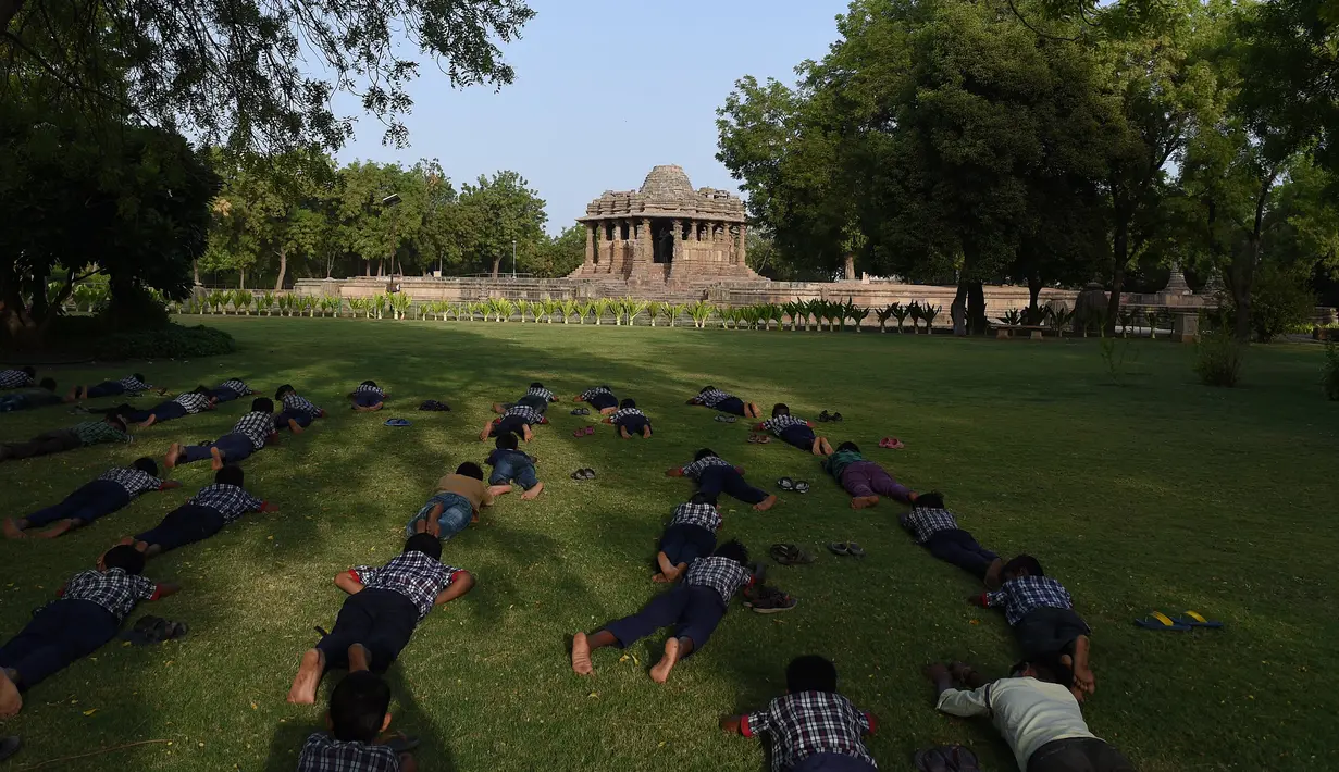 Para siswa terbaring saat  mengambil bagian dalam sesi yoga untuk menandai Hari Yoga Internasional di Kuil Matahari di Modhera, dekat kota Mahesana sekitar 100 km dari Ahmedabad di negara bagian Gujarat, (21/6). (AFP Photo/Sam Panthaky)