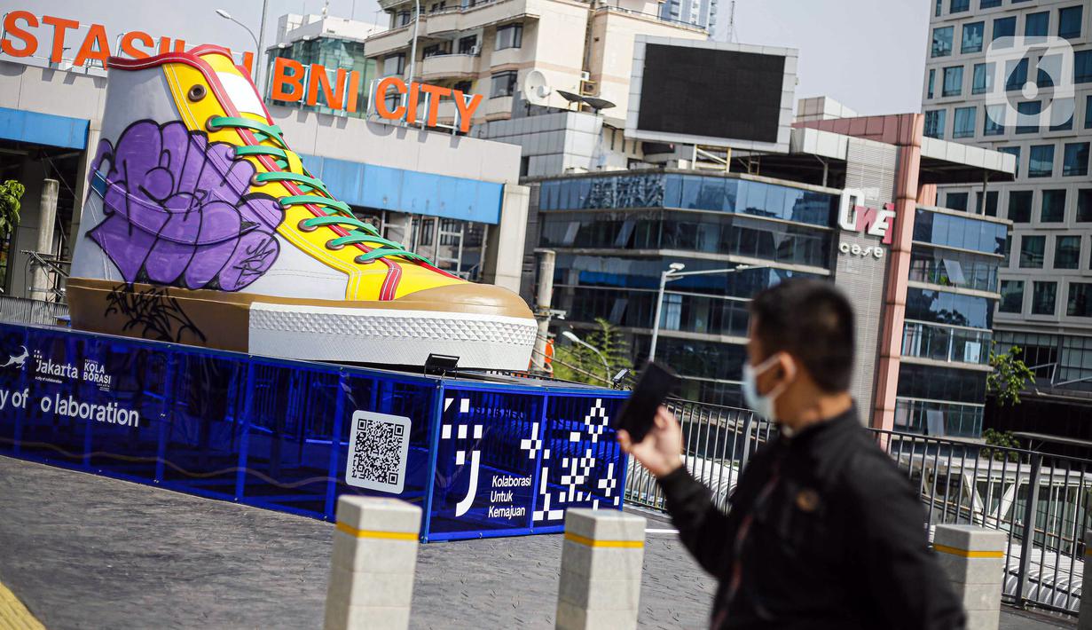 Pejalan kaki mengambil gambar Tugu Sepatu di Sudirman, Jakarta, Minggu (19/9/2021). Tugu Sepatu menjadi sasaran pencoretan dengan semprotan aerosol oleh orang tak dikenal sehari usai diresmikan pada 17 September 2021. (Liputan6.com/Faizal Fanani)