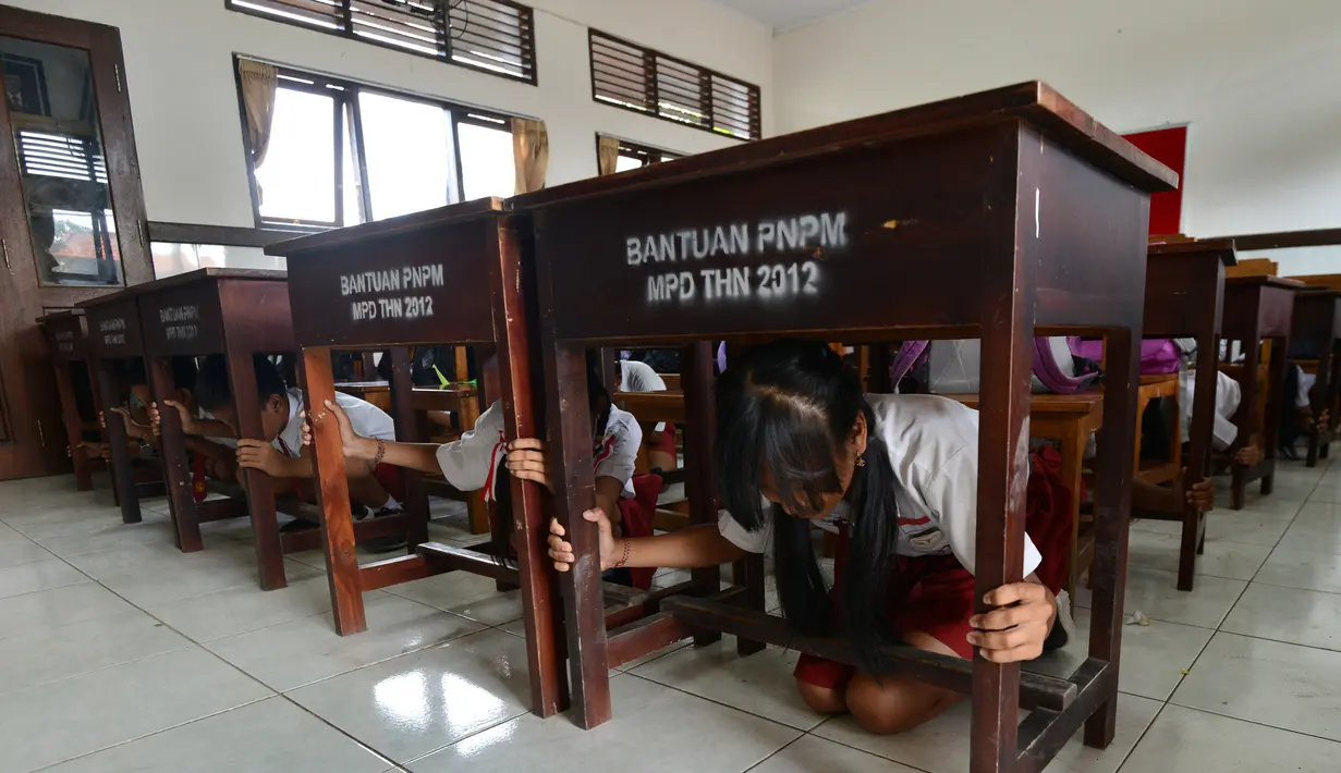 Sejumlah siswa SD berlindung di bawah meja selama latihan tsunami di Tanjung Benoa dekat Denpasar di pulau resor Bali (15/8). (AFP Photo/ Sonny Tumbelaka)