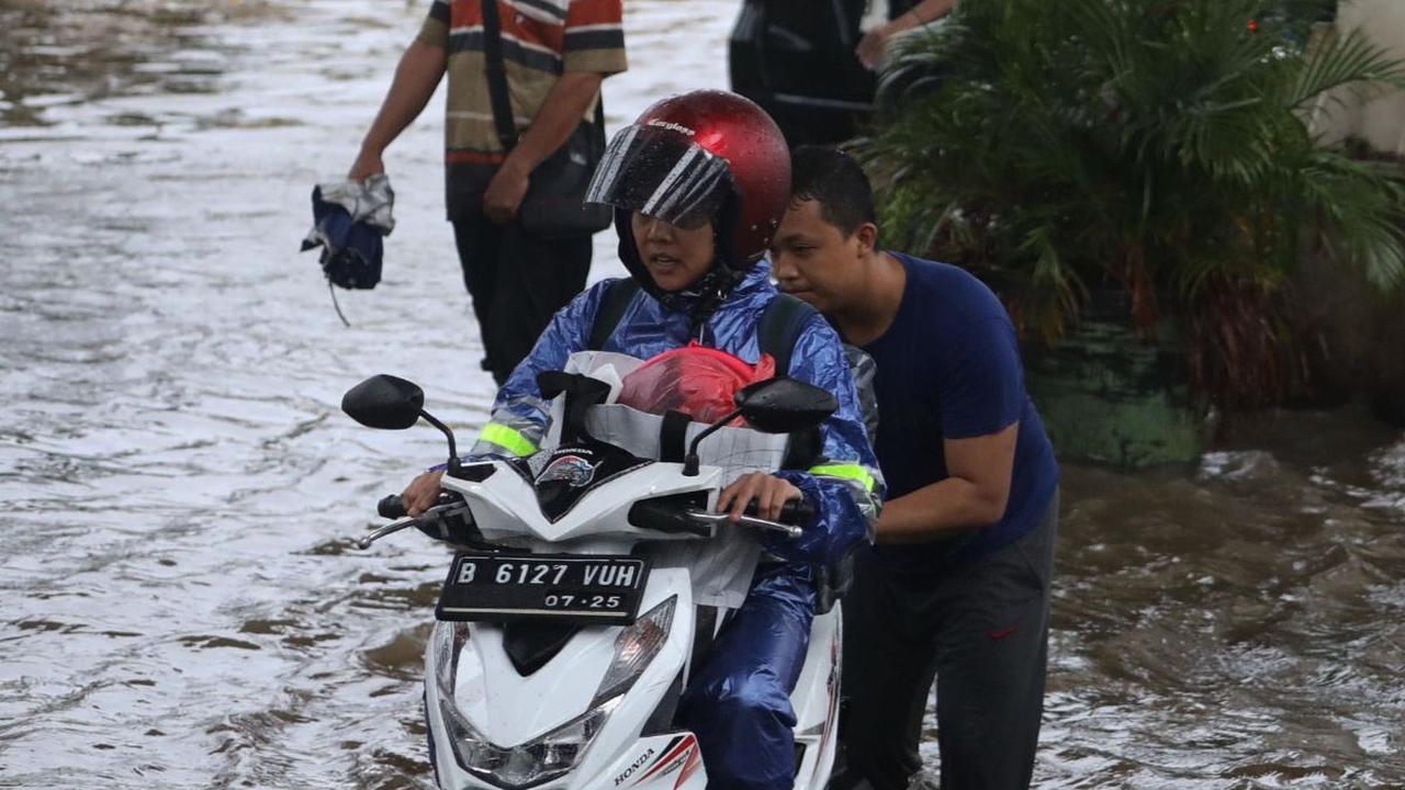 Seorang warga membantu pengendara melewati banjir yang merendam Jalan Ciledug Raya, Jakarta Selatan, Sabtu (6/7/2024).&nbsp; Liputan6.com/Angga Yuniar