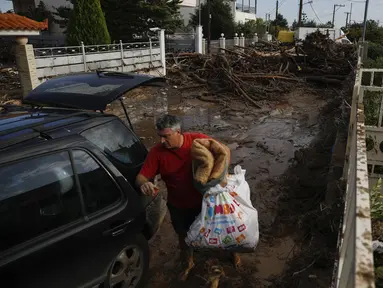 Seorang pria membawa barang miliknya dari rumahnya yang rusak ke mobilnya setelah badai di desa Kineta, Athena (25/11/2019). Pihak berwenang di Yunani mengatakan dua orang telah tewas dan ratusan lainnya luka-luka. (AP Photo/Petros Giannakouris)