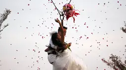 Sepasang pengantin membuang buket bunga sambil bergelantungan pada tali saat upacara pernikahan di Ratchaburi, Thailand, Sabtu (13/2). Upacara pernikahan tersebut diikuti empat pasang pengantin untuk menyambut Hari Valentine. (REUTERS/Athit Perawongmetha)