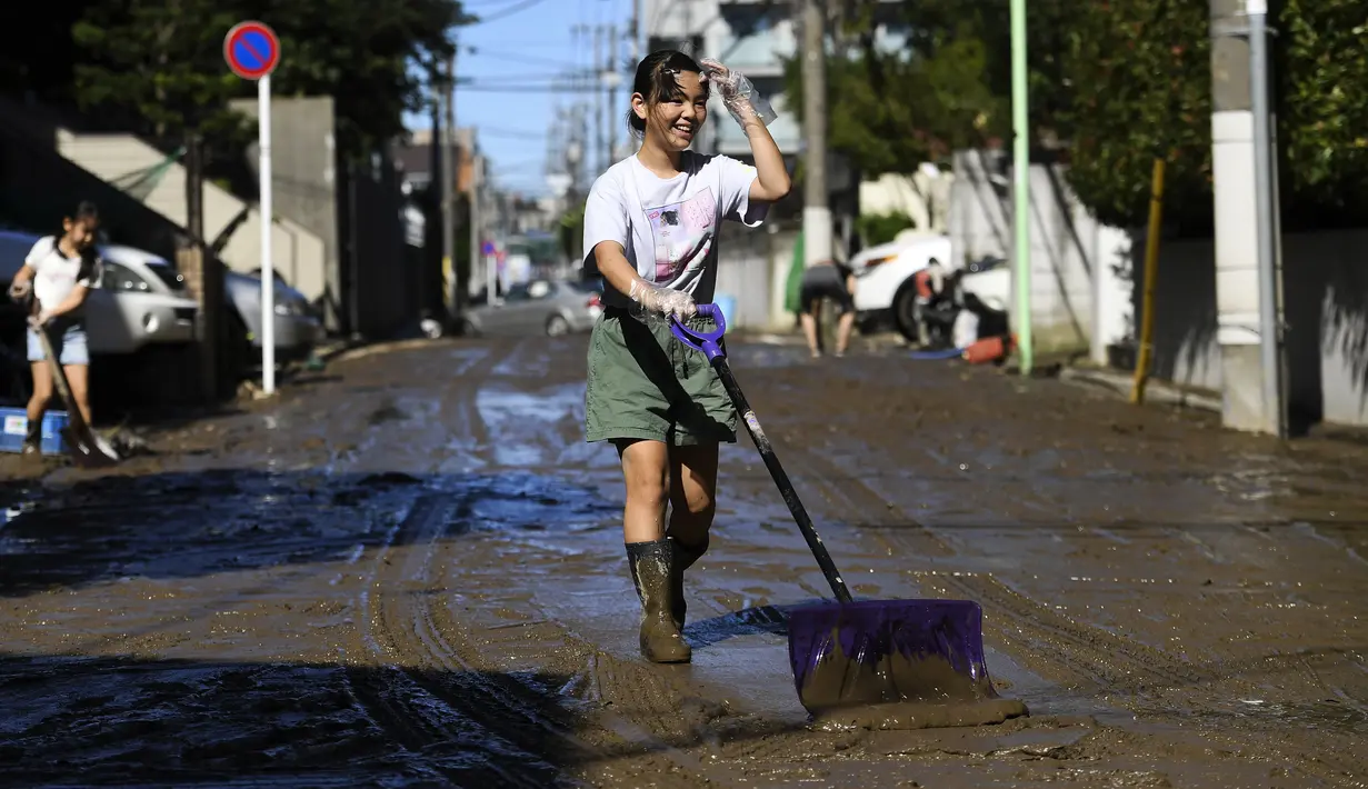 Seorang anak membersihkan lumpur dari jalan setelah banjir surut di Kawasaki, Minggu (13/10/2019). Topan dahsyat Hagibis yang menerjang sejumlah wilayah di Jepang menyebabkan banjir di beberapa lokasi. (Photo by WILLIAM WEST / AFP)