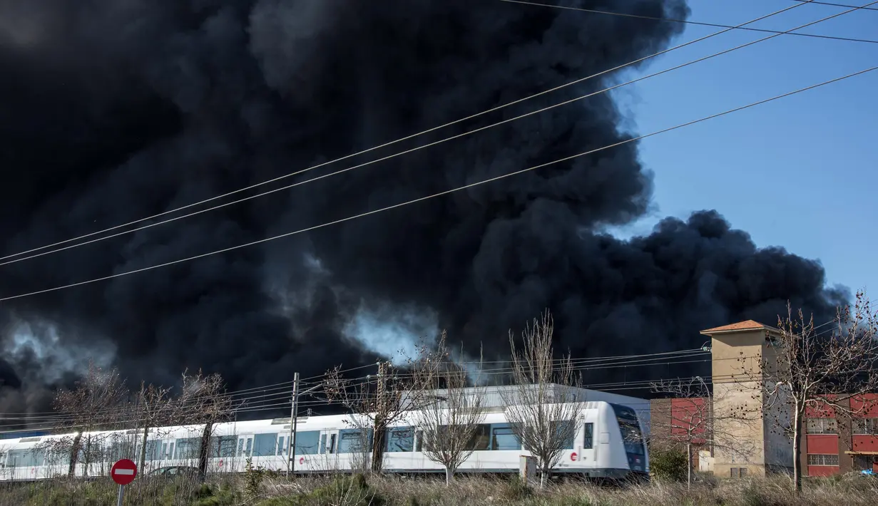 Kereta melintas di dekat perusahaan kimia Indukern yang sedang terjadi kebakaran di kawasan industri Fuente del Jarro, Paterna, Valencia, Spanyol, Rabu (8/2). (AFP PHOTO / Biel Alino)