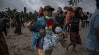 Seorang warga membawa seorang anak ketika orang-orang menyelamatkan barang-barang mereka di daerah yang tertutup abu vulkanik setelah letusan gunung berapi Semeru di desa Sumber Wuluh di Lumajang, Jawa Timur, Minggu (5/12/2021). (AFP /Juni Kriswanto)