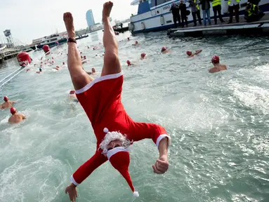 Seorang peserta dalam kostum sinterklas melompat ke air saat  kompetisi renang Copa Nadal di Port Vell Barcelona, Selasa (25/12). Lomba tradisional ini sudah menjadi tradisi lama yang mereka lakukan tiap tahun pada hari natal. (Josep LAGO / AFP)