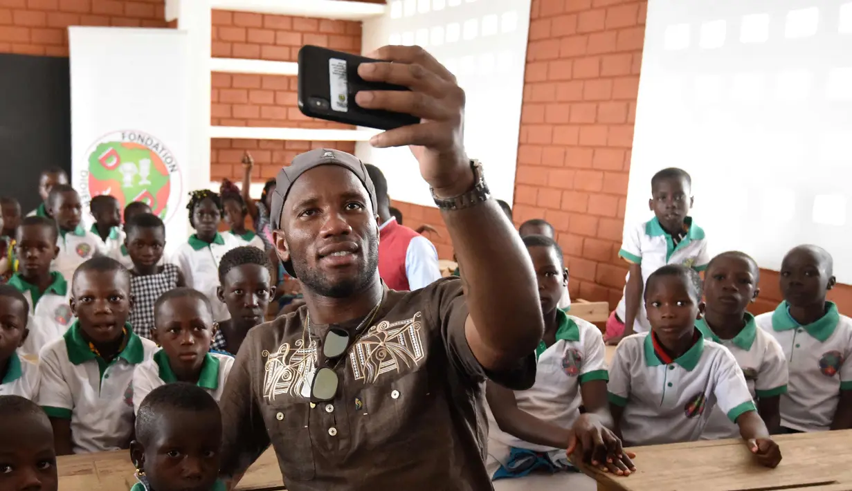 Mantan penyerang Chelsea, Didier Drogba berswafoto dengan murid-murid selama peresmian sekolah yang disponsori dirinya di Pokou-Kouamekro, dekat Gagnoa, Pantai Gading tengah barat (17/1). (AFP Photo/Sia Kambou)
