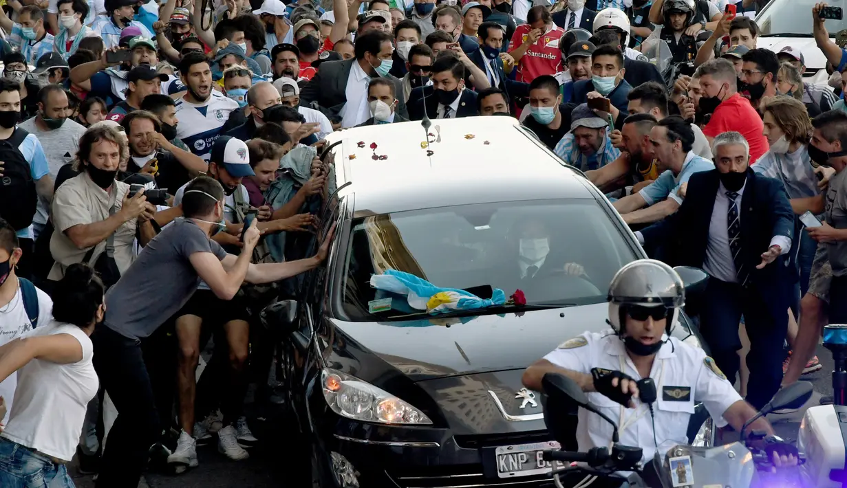 Para penggemar berkerumun di samping mobil jenazah yang membawa mendiang legenda sepak bola Argentina, Diego Maradona menuju pemakaman, di Buenos Aires, Kamis (26/11/2020).  Maradona meninggal dunia dalam usia 60 tahun pada Rabu (25/11) karena serangan jantung. (Raul FERRARI/TELAM/AFP)