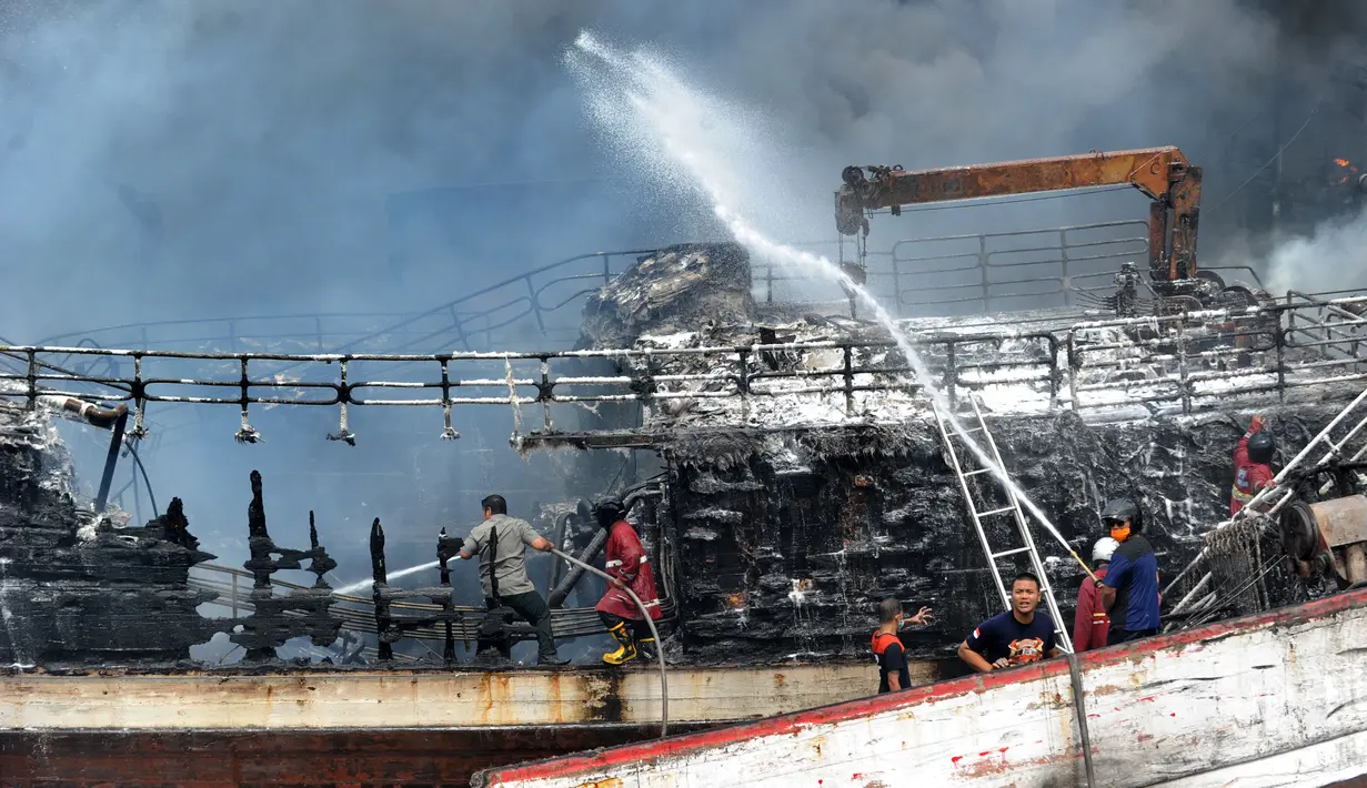 Petugas pemadam kebakaran dibantu pekerja mencoba memadamkan api di kapal nelayan di Pelabuhan Benoa, Denpasar, Bali, Senin (9/7). Hingga saat ini tak ada korban jiwa dalam kebakaran tersebut. (SONNY TUMBELAKA/AFP)