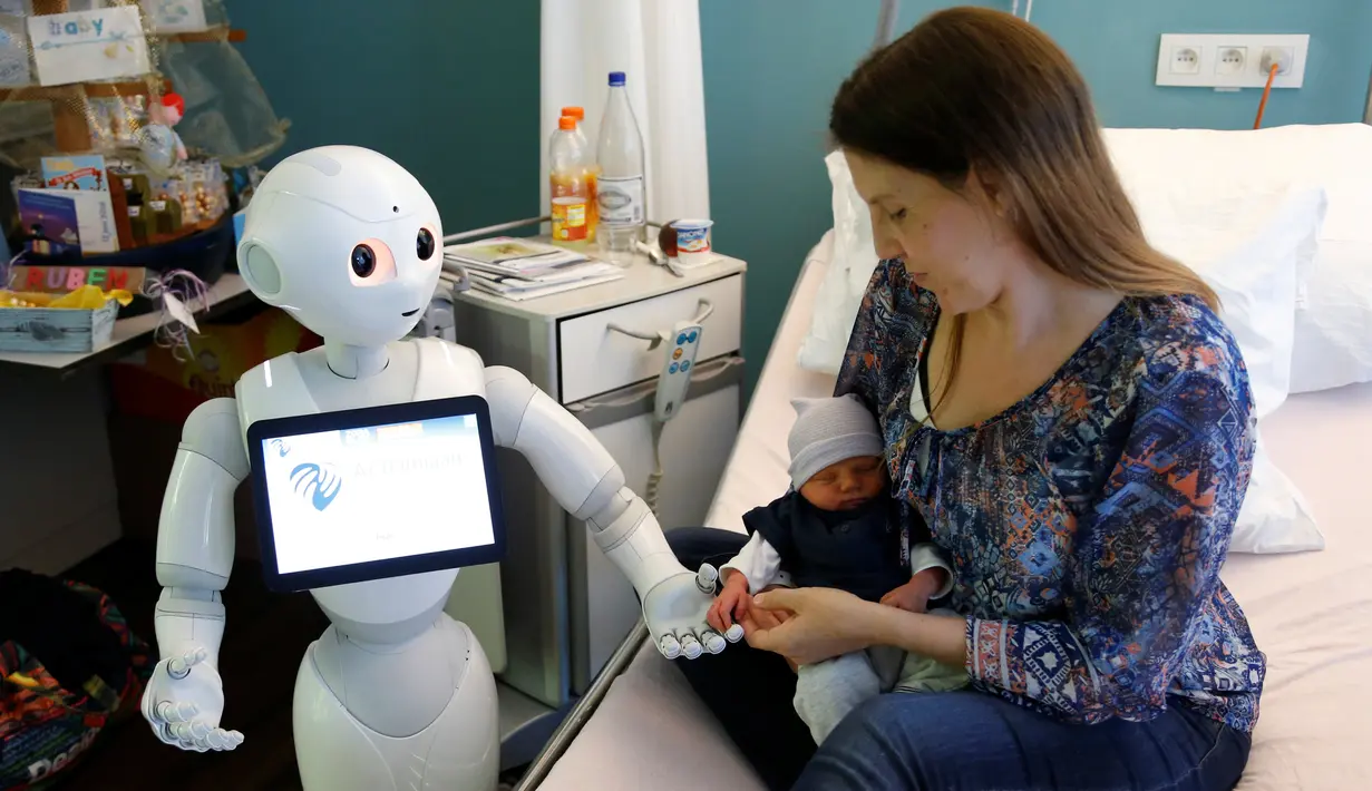 Robot humanoid bernama Pepper berdiri di samping seorang ibu dan bayinya yang baru lahir di rumah sakit AZ Damiaan di Ostend, Belgia (16/6). Robot dirancang atau dibuat untuk mengurus pasien yang datang ke rumah sakit ini. (REUTERS / Francois Lenoir)