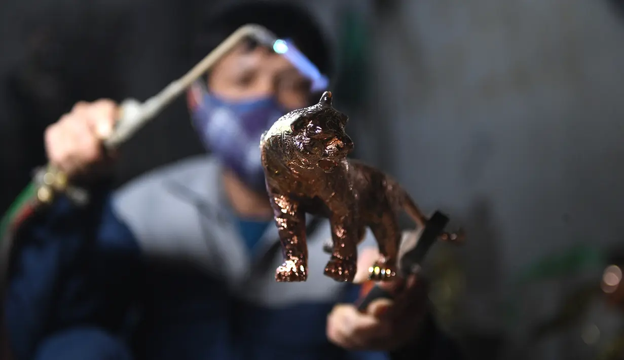 Pekerja membakar model harimau sebelum melapisinya dengan emas menjelang Tahun Baru Imlek, yang ditandai sebagai Tahun Macan Air di Hanoi pada 19 Januari 2022. Di Vietnam, perayaan Tahun Baru China disebut Tet yang merupakan salah satu perayaan paling penting masyarakat di sana. (Nhac NGUYEN/AFP)