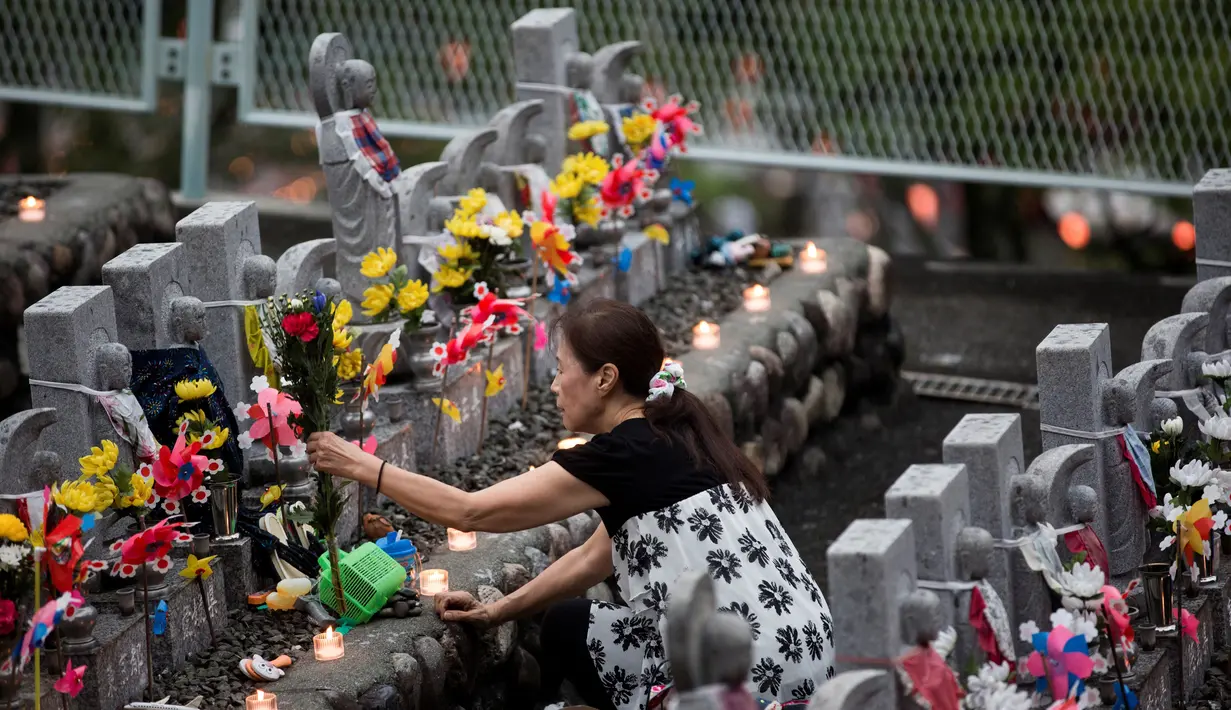 Seorang wanita menaruh bunga di depan patung Jizo yang didedikasikan untuk jiwa anak-anak yang telah meninggal dunia di Kuil Buddha Jizoji, Oganomachi, Prefektur Saitama, Jepang, Senin (13/8). (Behrouz Mehri/AFP)