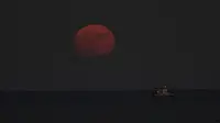 Bulan purnama terbit di atas laut Mediterania saat kapal nelayan melintas, di kota pesisir selatan Larnaca, di pulau tenggara Siprus, pada Rabu (13/7/2022). Bulan Purnama dikenal sebagai Buck Moon dan juga Supermoon. Di kondisi ini Bulan akan terlihat tampak lebih besar dan terang sehingga terasa sangat dekat dari Bumi. (AP Photo/Petros Karadjias)