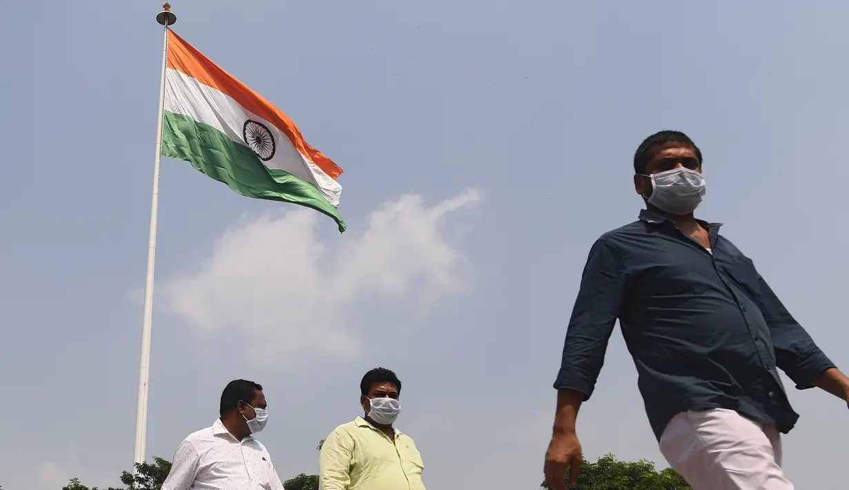 Sejumlah pria mengenakan masker berjalan melewati bendera nasional India di New Delhi (16/9/2020). Total kasus Covid-19 di India melampaui lima juta pada 16 September, data kementerian kesehatan menunjukkan Pandemi meluas cengkeramannya di negara tersebut. (AFP/Sajjad Hussan)