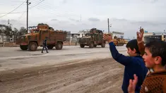 Sejumlah anak-anak melambaikan tangan ke iring-iringan pasukan lapis baja Turki (APC) yang melewati persimpangan perbatasan Bab al-Salamah antara Suriah dan Turki di utara provinsi Aleppo (21/1). (AFP/ Nazeer al-Khatib)