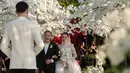 Gaun berwarna putih gading tersebut hadir dengan siluet ball gown yang megah. Bagian atasnya dirancang dengan high neckline dan lengan panjang transparan berbahan lace yang dihiasi detail payet berkilau. Permainan tekstur tulle, embroidery, dan taburan kristal menciptakan dimensi yang membuat gaun terlihat mewah dari setiap sudut. [@jennifercoppenreal20].
