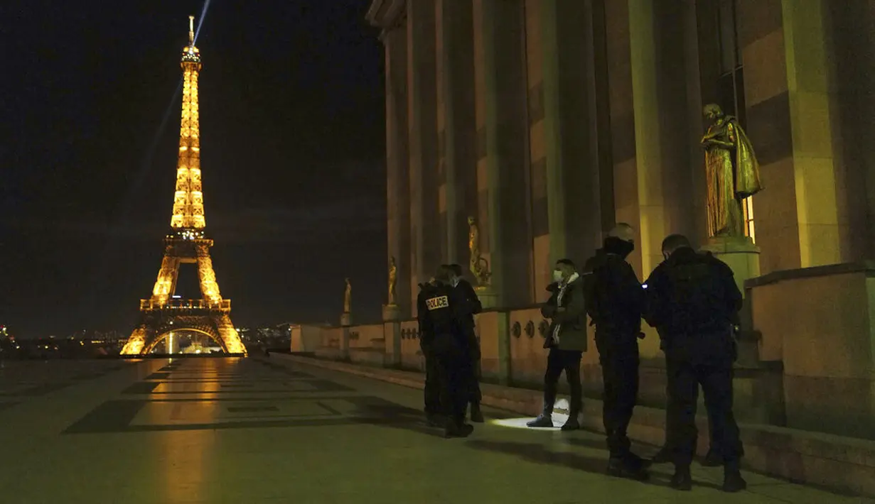 Polisi memeriksa seseorang selama jam malam di Trocadero, dekat Menara Eiffel, Paris, Perancis, Selasa (15/12/2020). Para pejabat telah memperingatkan bahwa mereka akan menegakkan peraturan baru dengan ketat. (AP Photo/Francois Mori)