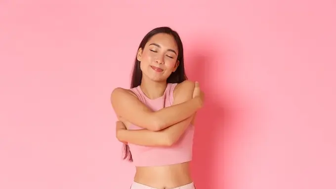 Seorang perempuan berbaju pink tampak memeluk dirinya sendiri (Foto Dok: Freepik/benzoix)