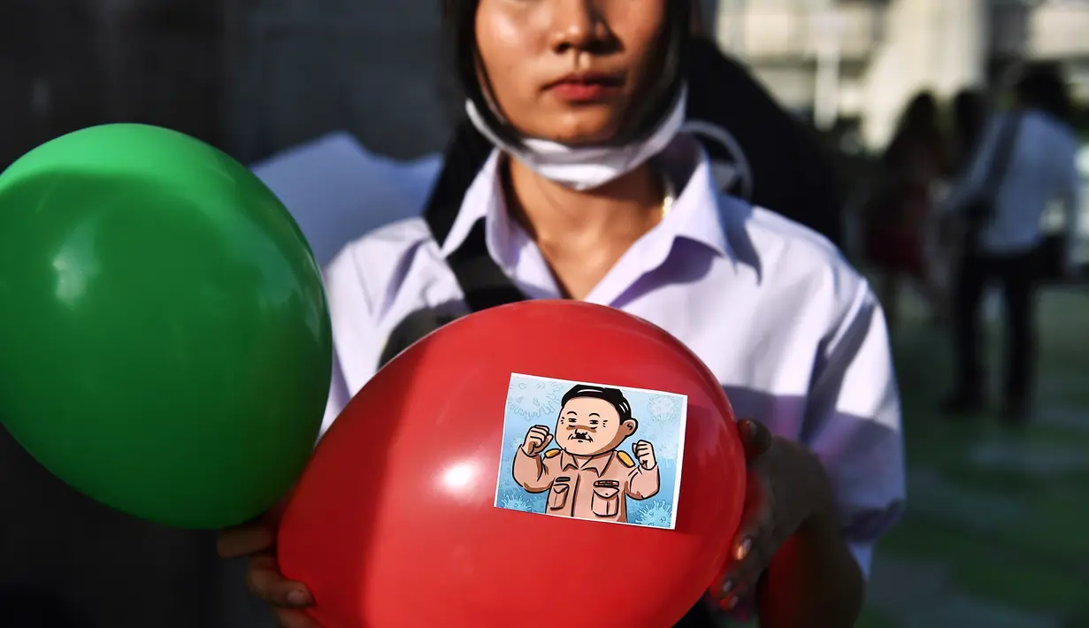Seorang pengunjuk rasa memegang balon, dengan stiker yang menggambarkan Perdana Menteri Thailand Prayut Chan-O-Cha sebagai Adolf Hitler, selama demonstrasi menentang usulan pembelian kapal selam oleh pemerintah yang berpihak pada militer di Bangkok (31/8/2020). (AFP/Lillian Suwanrumpha)