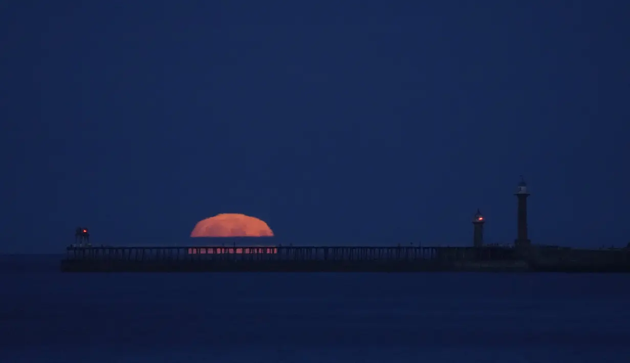 Bulan purnama yang dikenal sebagai Harvest moon terbit di atas pelabuhan Whitby, di Whitby, Inggris, Senin (20/9/2021). Bulan purnama Harvest Moon biasanya terjadi di bulan September, namun kadang juga terlambat hingga ke Oktober. (AP Photo/Alastair Grant)