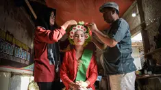 Seorang perempuan dengan pakaian tradisional dibantu menyiapkan hiasan bunga di rambutnya untuk berpartisipasi dalam Festival Ngarot di Lelea, Indramayu , Jawa Barat, pada 13 Desember 2023. (Timur MATAHARI/AFP)