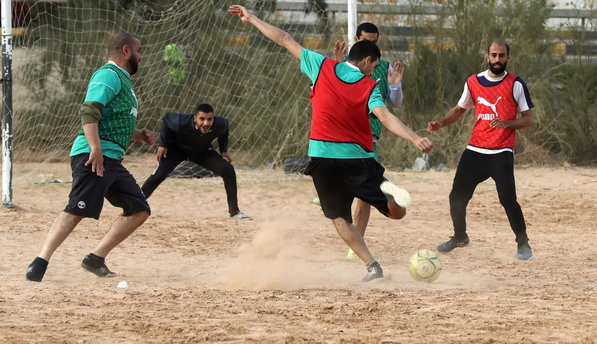 Seorang pemain menembak bola saat bermain di lapangan tanah sebelum buka puasa selama bulan Ramadhan, di ibu kota Libya, Tripoli (24/4/2021). (AFP/Mahmud Turkia)