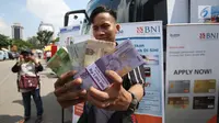 Warga menunjukkan uang pecahan yang ditukarkan dari mobil kas keliling di Lapangan IRTI Monas, Rabu (7/6). Bank Indonesia dan 13 bank umum membuka gerai penukaran uang pecahan dengan penukaran maksimal Rp3,7 juta per orang. (Liputan6.com/Angga Yuniar)