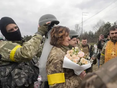 Seorang tentara memegang helm sebagai tiara mahkota pada upacara pernikahan anggota Pasukan Pertahanan Teritorial Ukraina Lesia Ivashchenko dan Valerii Fylymonov di pos pemeriksaan di Kiev, 6 Maret 2022. Kedunya menikah dengan upacara seadanya yang dilakukan korps mereka. (AP/Efrem Lukatsky)