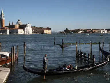 Seorang gondolier mendayung gondola di dekat gereja Santa Maria della Salute di Venesia pada 20 Mei 2021. Turis kembali berdatangan menikmati keindahan Venesia, yang sering dijuluki kota paling romantis di dunia, setelah Italia menghapus kewajiban karantina bagi pendatang. (Marco Bertorello/AFP)