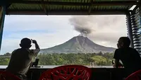 Dua pria menyaksikan Gunung Sinabung menyemburkan abu dan asap tebal dari wilayah Karo, Provinsi Sumatra Utara, Rabu, 2 September 2026. (AFP/ YT Haryono)